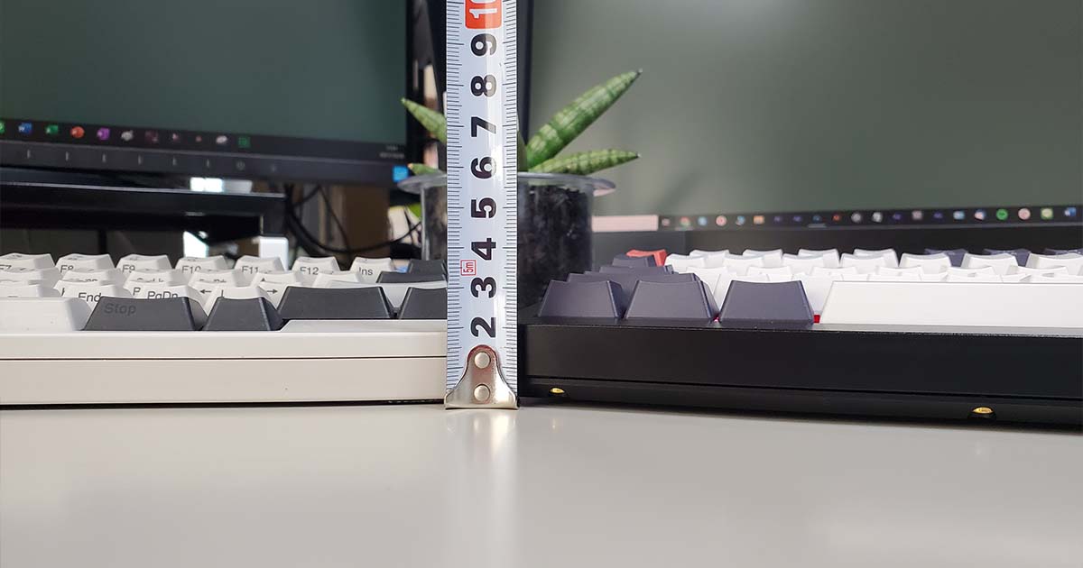 メジャーを立ててHHKBとKeychron Q1の高さを実測しているデスク上の比較写真